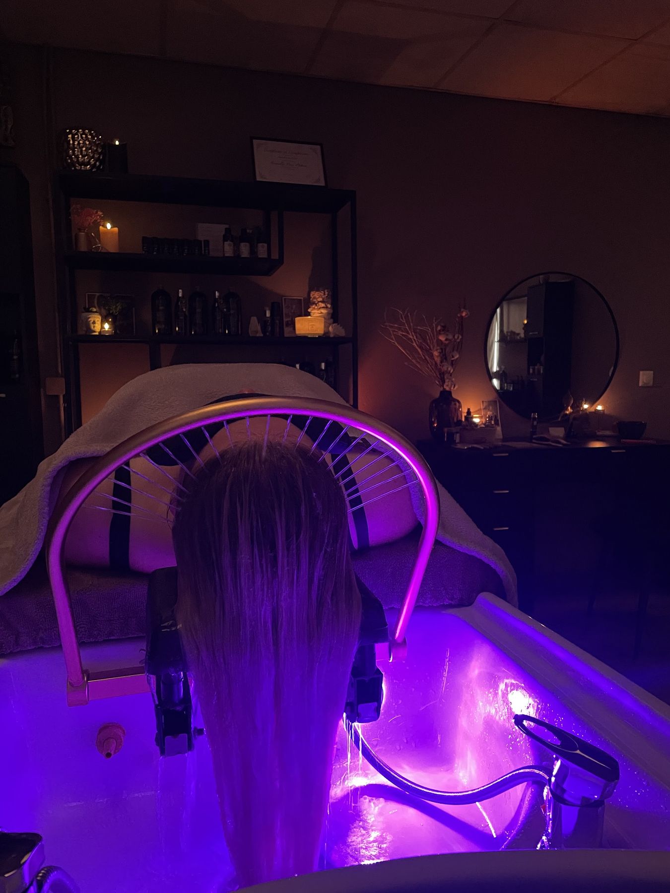 Een klant ligt met haar haren onder de verlichte waterboog van de headspa, in een donkere ruimte met kaarsen