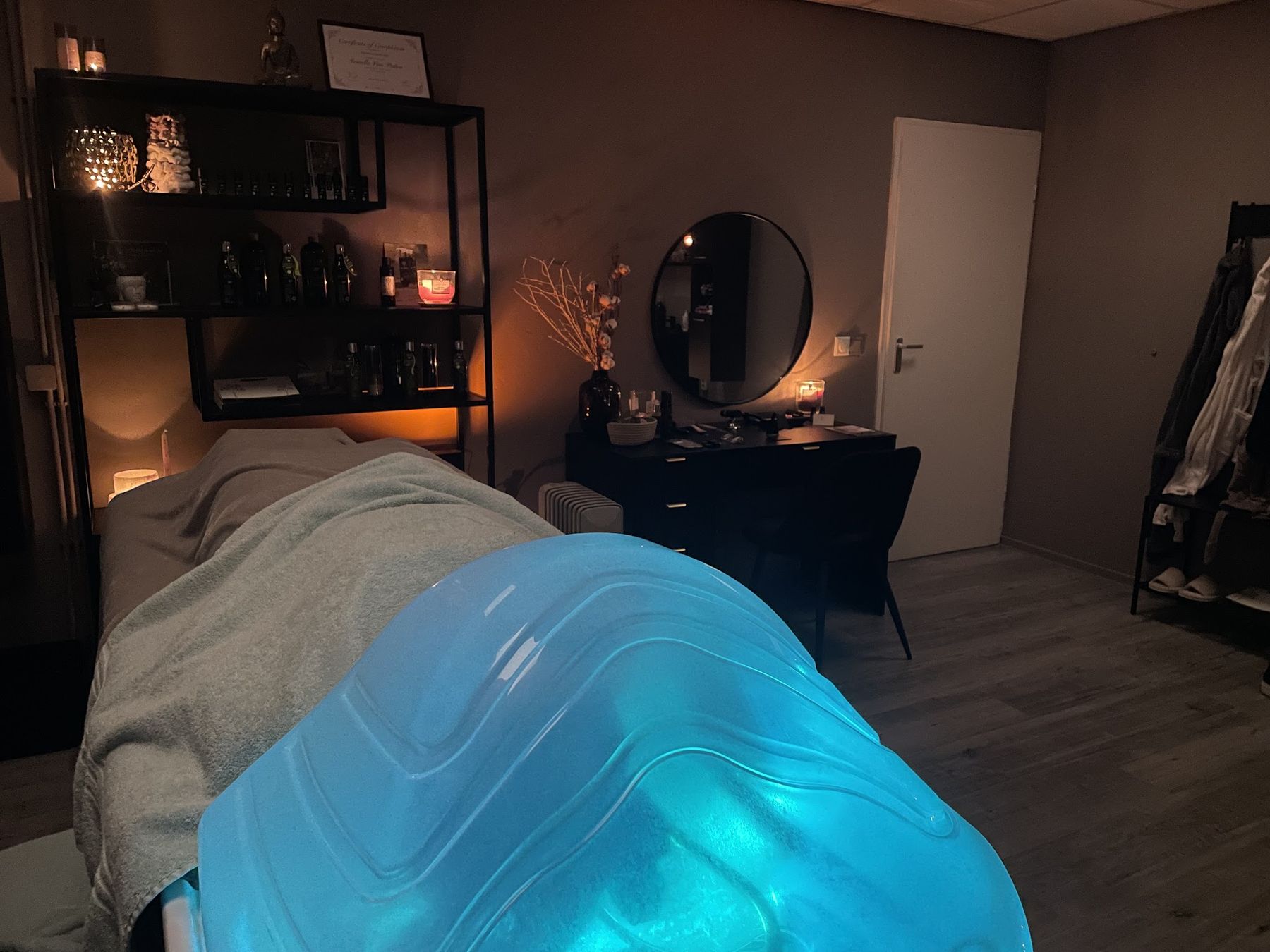 De behandelruimte: een behandeltafel met een blauw verlichte waskom, kaarsen op de kasten en een ronde spiegel